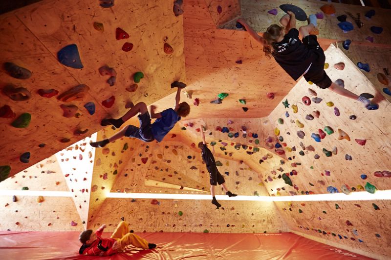 Several young climbers are training in the bouldering room. They are climbing up the walls and ceiling, and one of them has just fallen onto the protective mat below